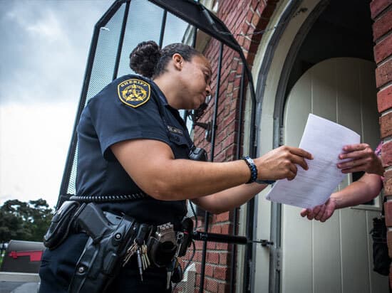 Female Deputy Handing Warrant to Hand in Doorway